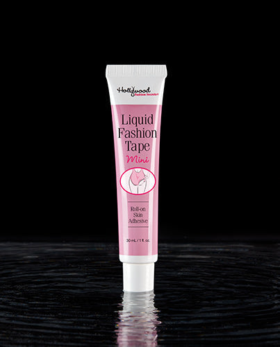A pink and white tube of Hollywood Fashion Secrets Liquid Fashion Tape Mini roll-on skin adhesive stands on a reflective dark surface.