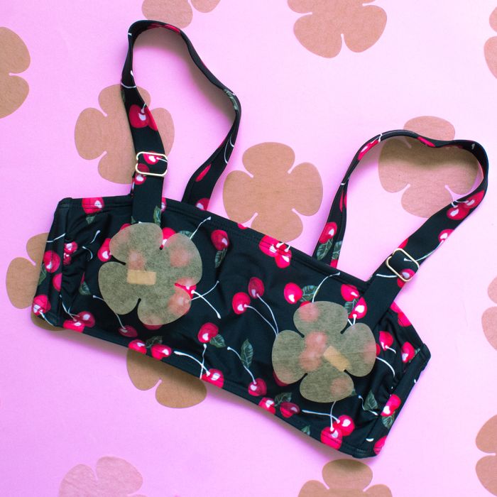A black cherry print bikini top features translucent flower-shaped pasties against a bright pink background with matching floral accents.