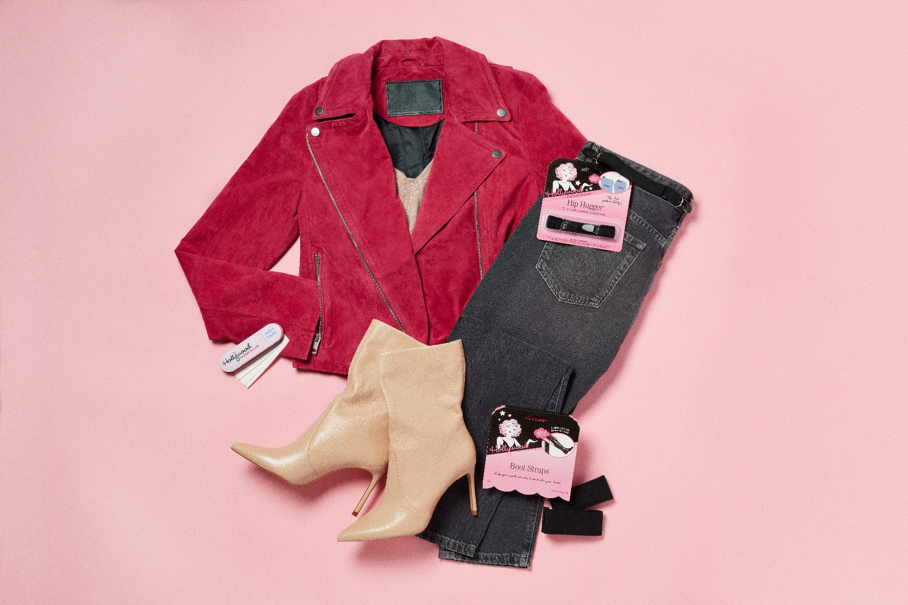 A stylish flat lay displays a red suede moto jacket, dark gray denim jeans, and beige stiletto ankle boots paired with Hollywood Fashion Secrets fit accessories on a pink background.