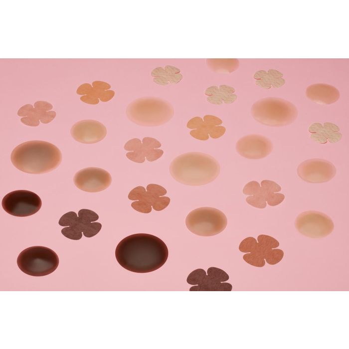 An assortment of flower-shaped and circular adhesive nipple covers in diverse skin tones sits on a pink background.