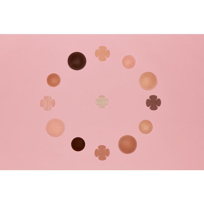 An inclusive collection of adhesive nipple covers and clover pasties in various skin tones forms a circle on a light pink surface.