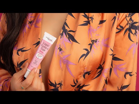 A woman holds a tube of Hollywood Fashion Secrets Liquid Fashion Tape Mini against her orange floral robe to demonstrate how to secure clothing.