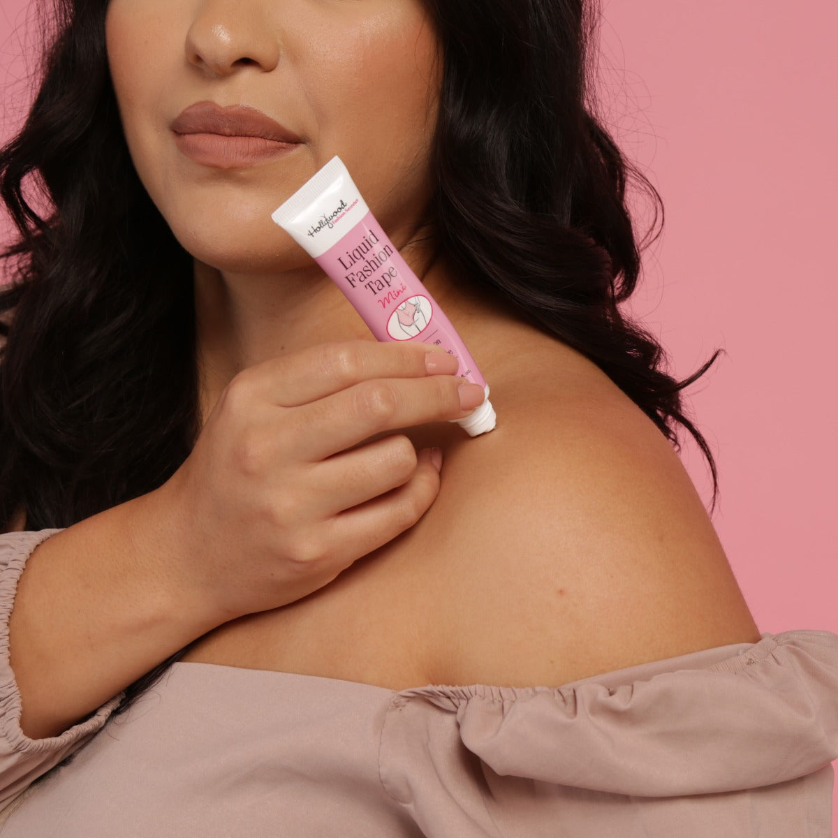 A woman applies Hollywood Fashion Secrets Mini Liquid Fashion Tape to her shoulder to secure an off-the-shoulder top.