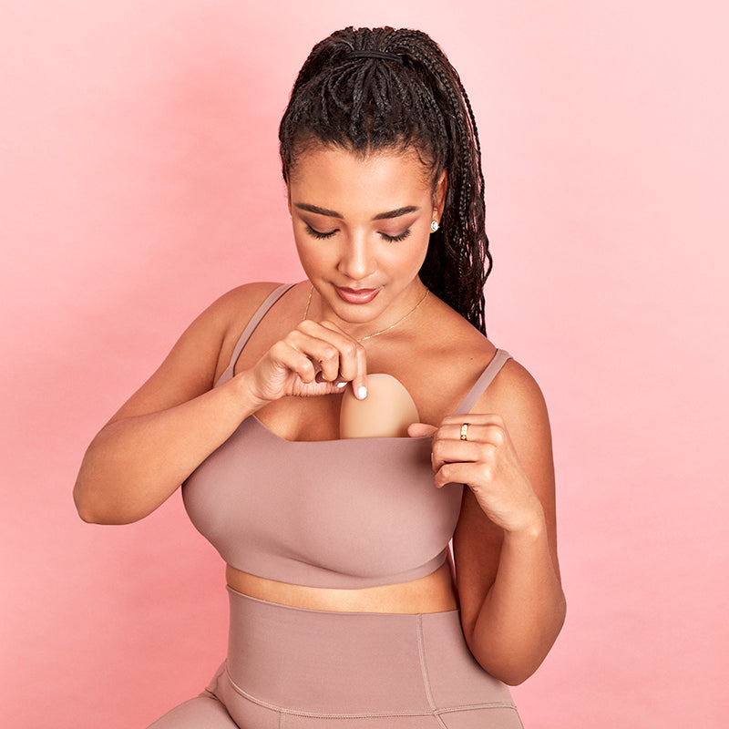 Woman in a matching sports bra and leggings set holding a beige object against a pink background