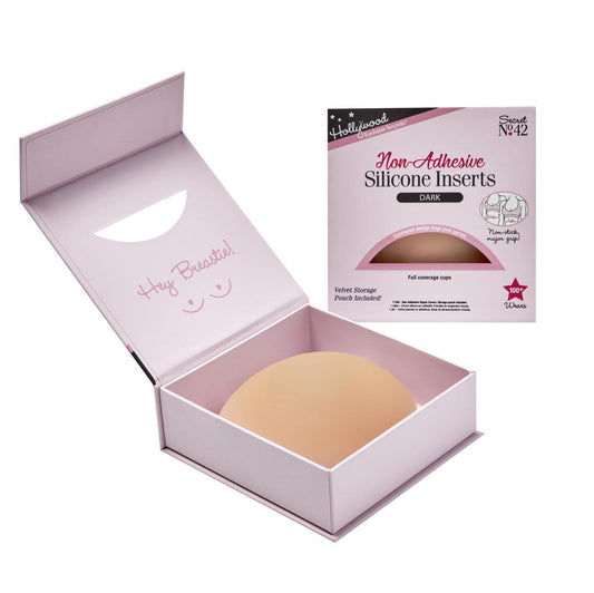 A pair of Hollywood Fashion Secrets non-adhesive silicone breast inserts in a dark shade rests inside an open pink storage box next to its retail packaging.