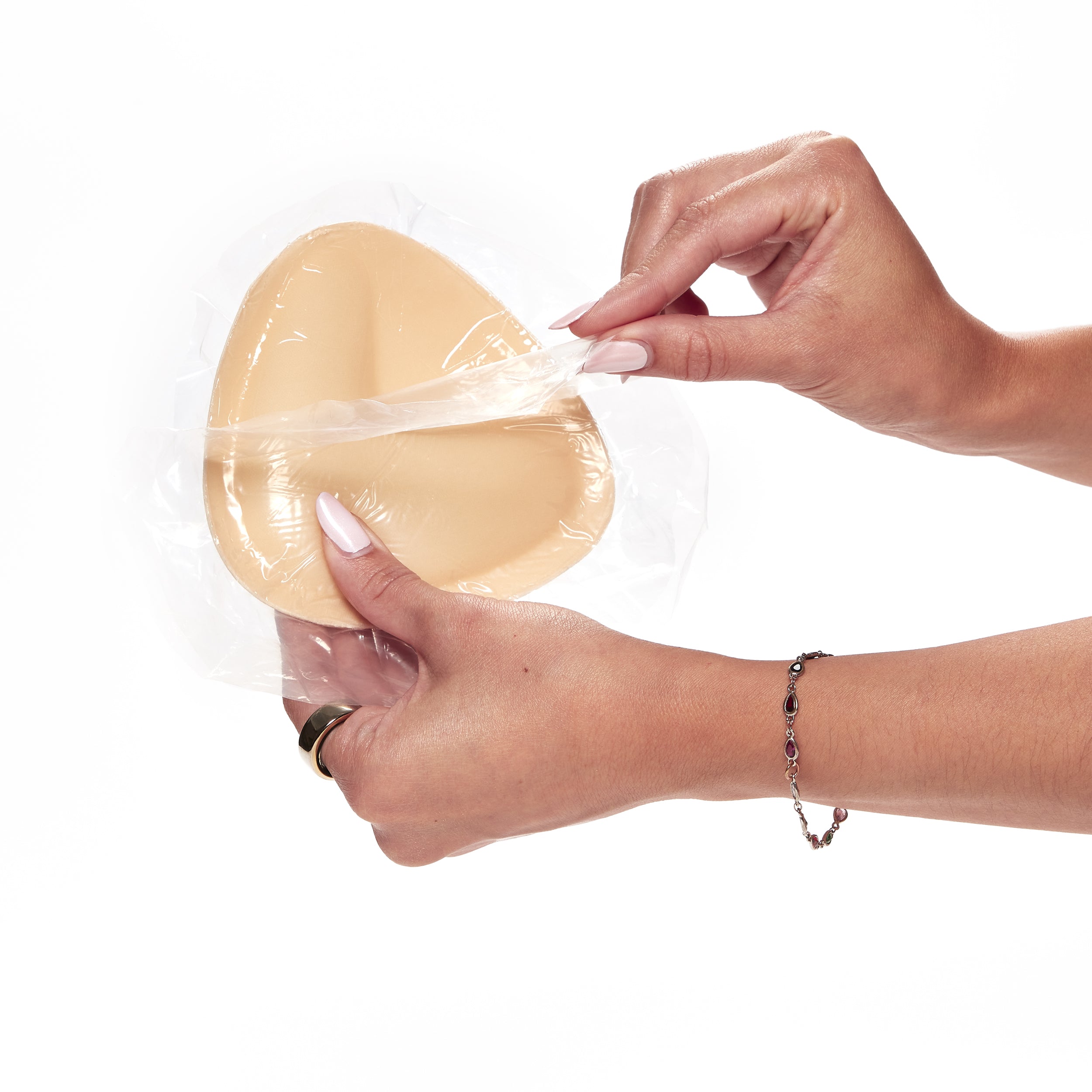 Person holding a silicone breast implant with clear plastic wrap on a white background