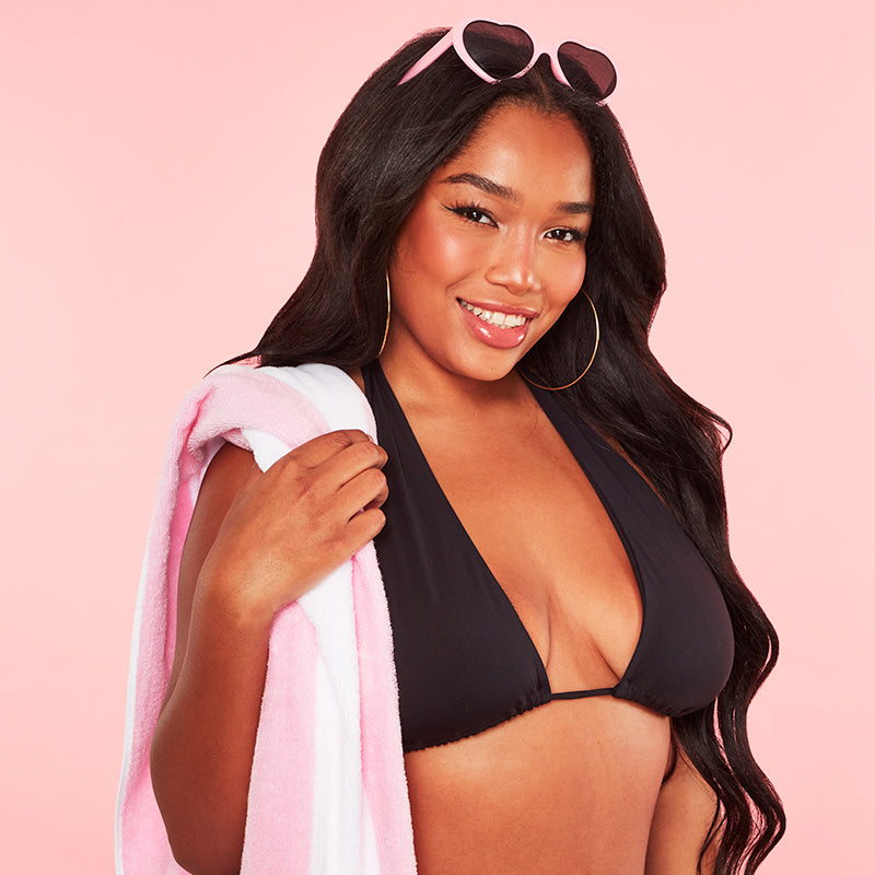 Woman in a black bikini holding a pink towel against a pink background