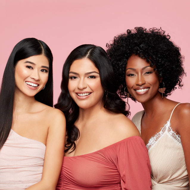 Diverse Women Smiling – Three diverse women in fashionable outfits posing against a pink background.