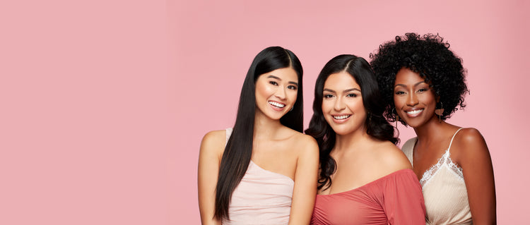 Diverse Women Smiling – Three diverse women in fashionable outfits posing against a pink background.