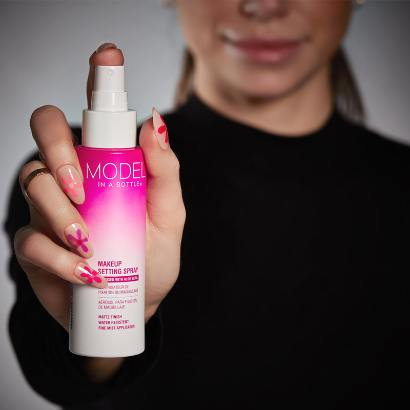 Person holding a pink makeup setting spray bottle with 'Model in a Bottle' branding.