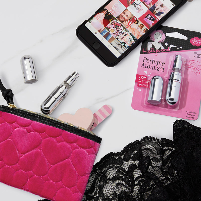 Perfume atomizers, pink pouch, and black lace on a white surface with a phone displaying images.