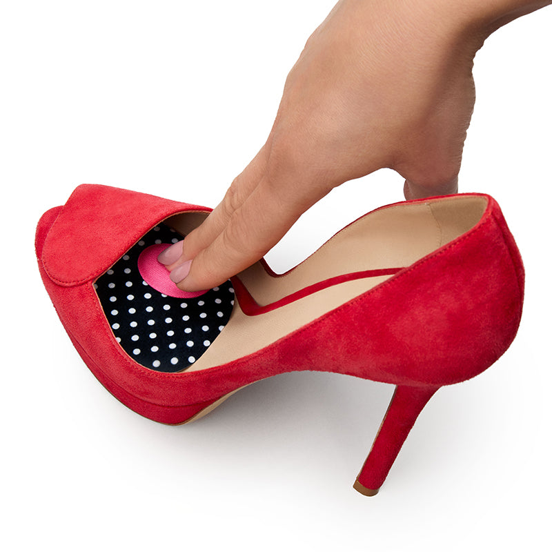 Red high-heeled shoe with a hand inserting a polka dot object into the shoe on a white background