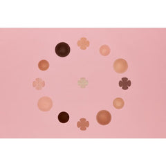 An inclusive collection of circular and floral nipple covers in diverse skin tones forms a circular pattern on a pink background.