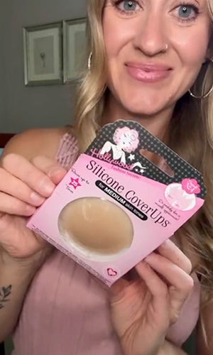 A woman holding a pink package of silicone coverups, showing the beige silicone cup through a clear window on the front of the packaging.