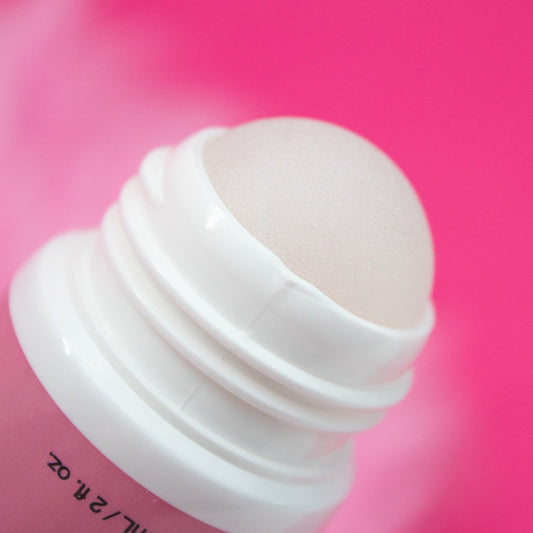 A white roll-on deodorant applicator with a smooth roller ball and threaded neck rests against a vibrant pink background.