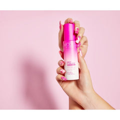 Hand holding Model in a Bottle Makeup Setting Spray against a pink backdrop, highlighting product size and packaging.